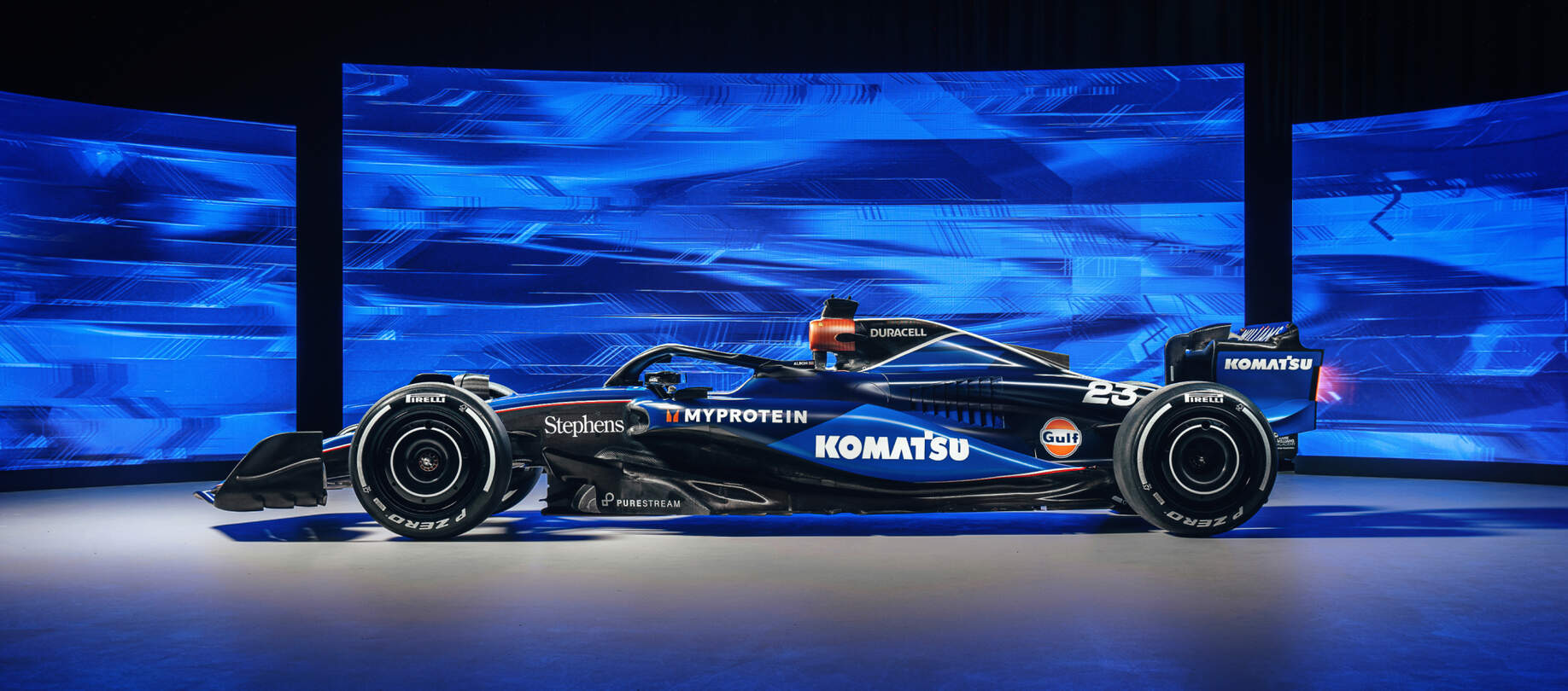 A sleek, modern Formula 1 race car is showcased in a studio setting with a vibrant blue and black digital background.