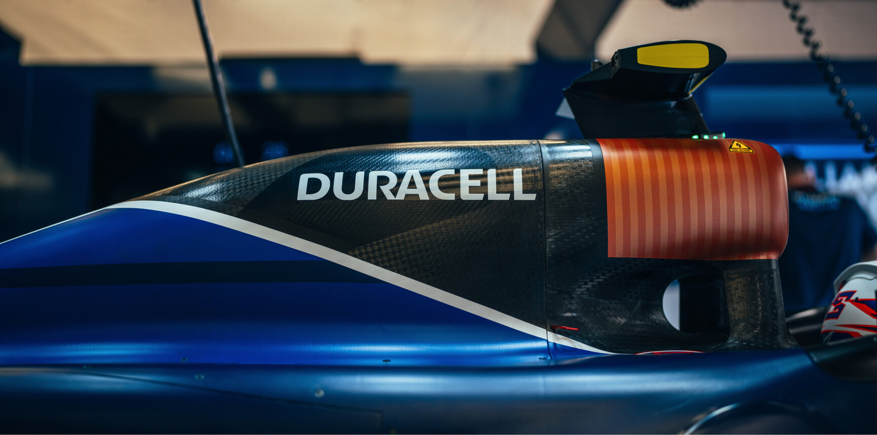 Close-up side view of a Williams Racing Formula 1 car's air intake and bodywork. The car prominently displays the Duracell logo on the carbon fiber structure. The air intake is designed to resemble a Duracell battery with a copper top. The image highlights the detailed design and sponsor integration on the car.