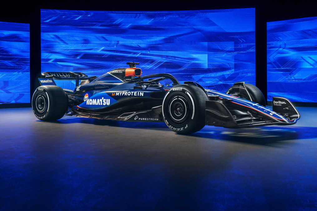 Side view of a Williams Racing Formula 1 car showcased in a studio with blue background lighting. The car features prominent branding from Duracell. The sleek design of the car is highlighted, with its aerodynamic shape and detailed sponsor logos clearly visible on the bodywork and tires.