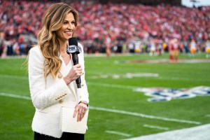 A sideline reporter films a hit at an NFL game.