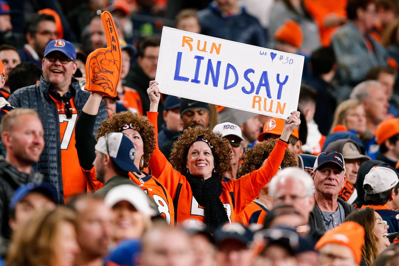 A woman wearing a wig resembling Denver Broncos running back Phillip Lindsay's hair holds a sign reading "Run Lindsay Run."