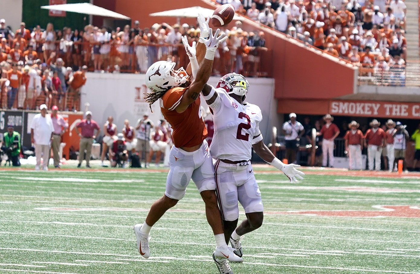 Two NCAA college football players reach for a pass.