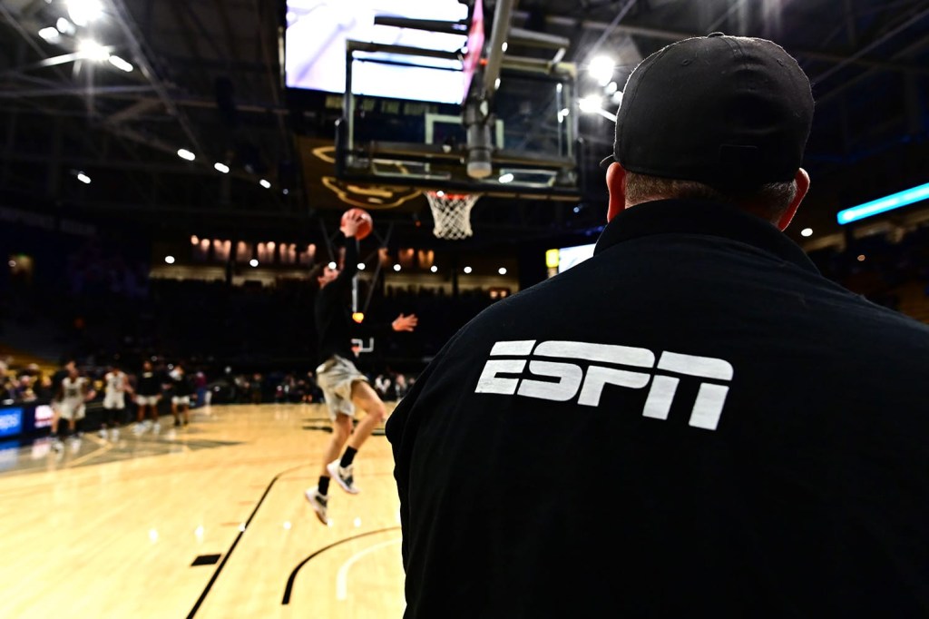 Man wearing ESPN logo on back of shirt while court side at mens college basketball game