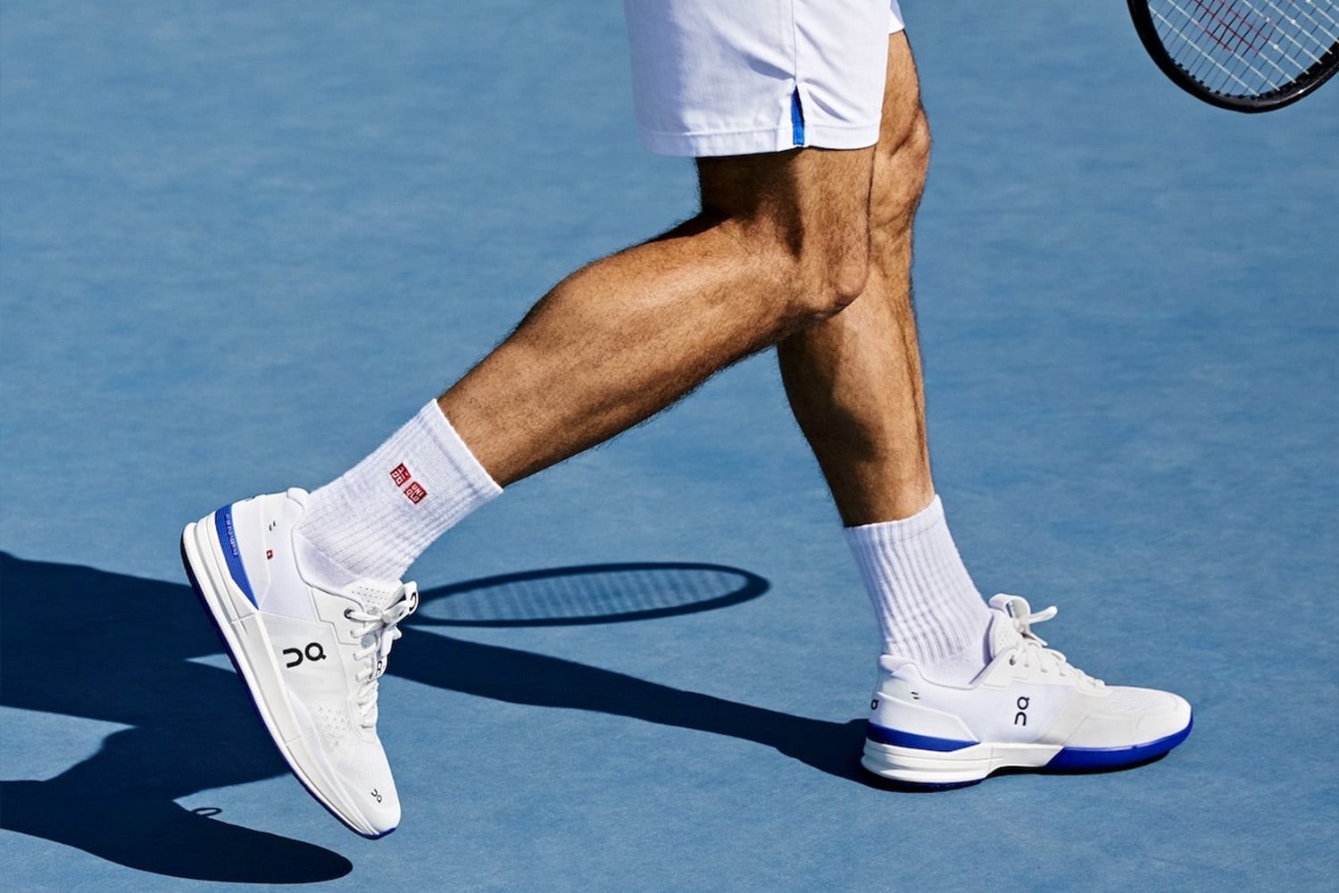 Legs of male tennis player wearing white tennis shoes and Uniqlo socks