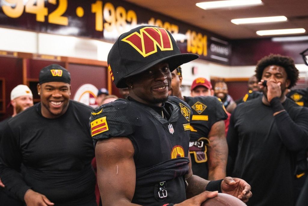 Washington Commanders running back Brian Robinson wears large hat while celebrating with teammates after game