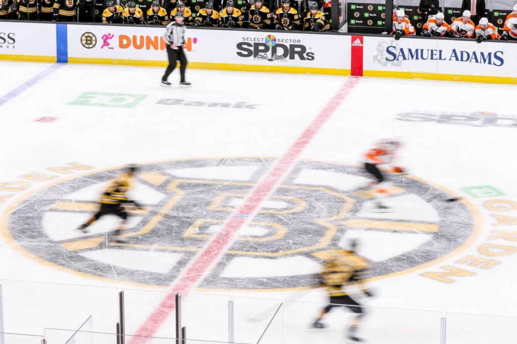 Players skate past Bruins logo at center ice in match up between Boston Bruins and Philadelphia Flyers