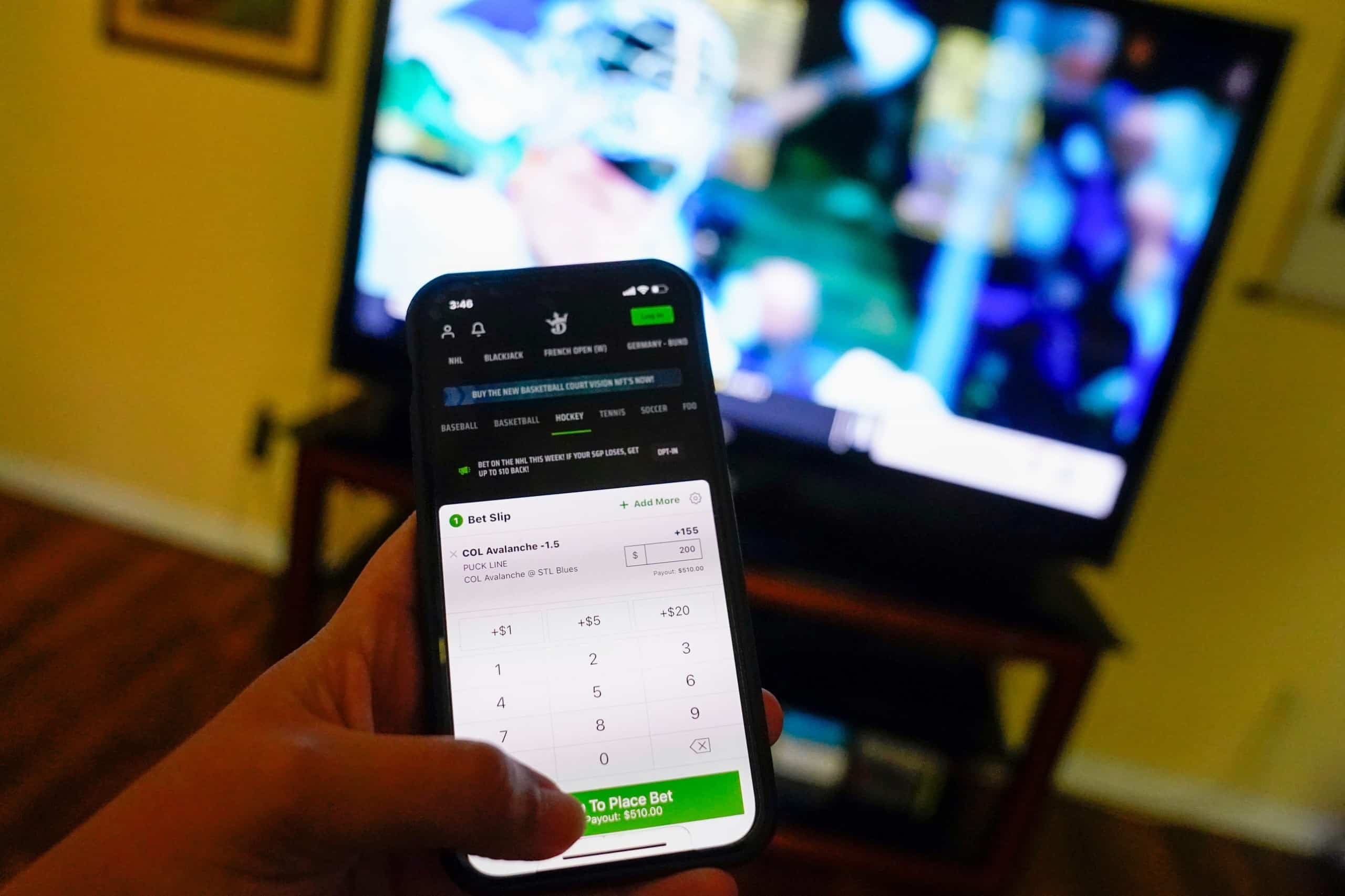 Person using Draft Kings app while watching sports on TV