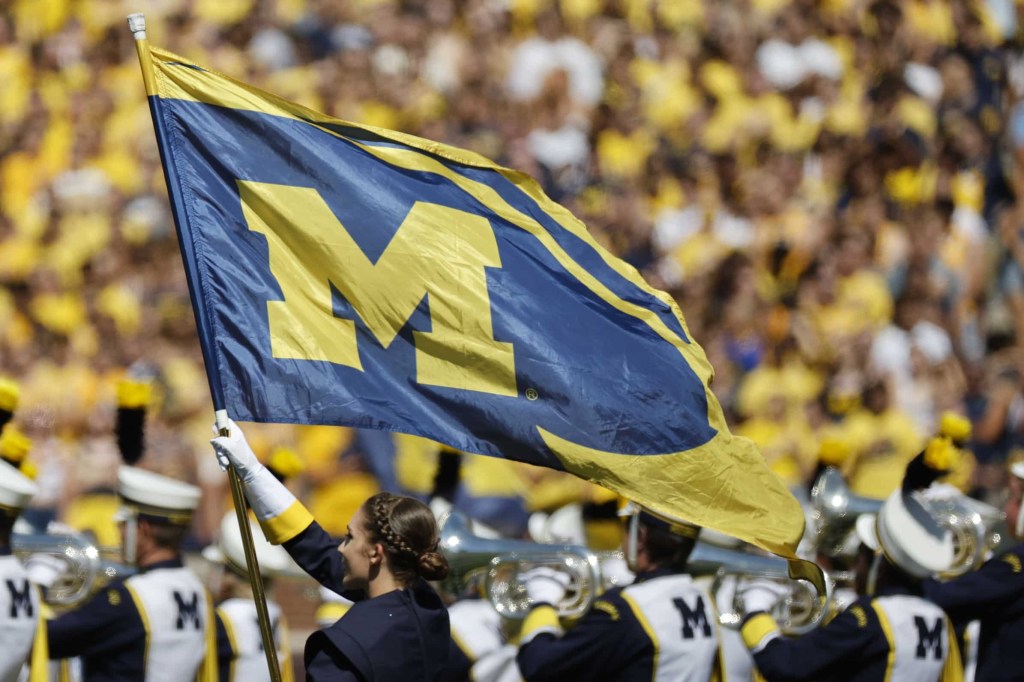 Member of University of Michigan band waives flag with block M and iconic helmet design ahead of football game