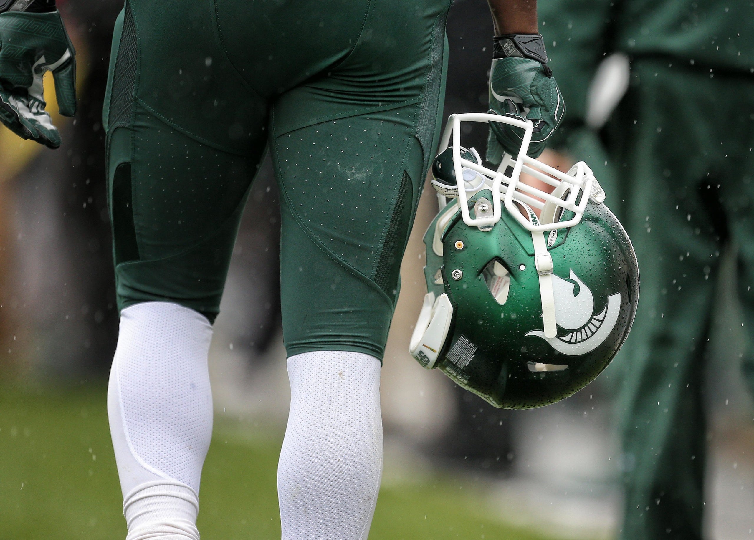 Photo of Michigan State football player holding helmet at knee-level