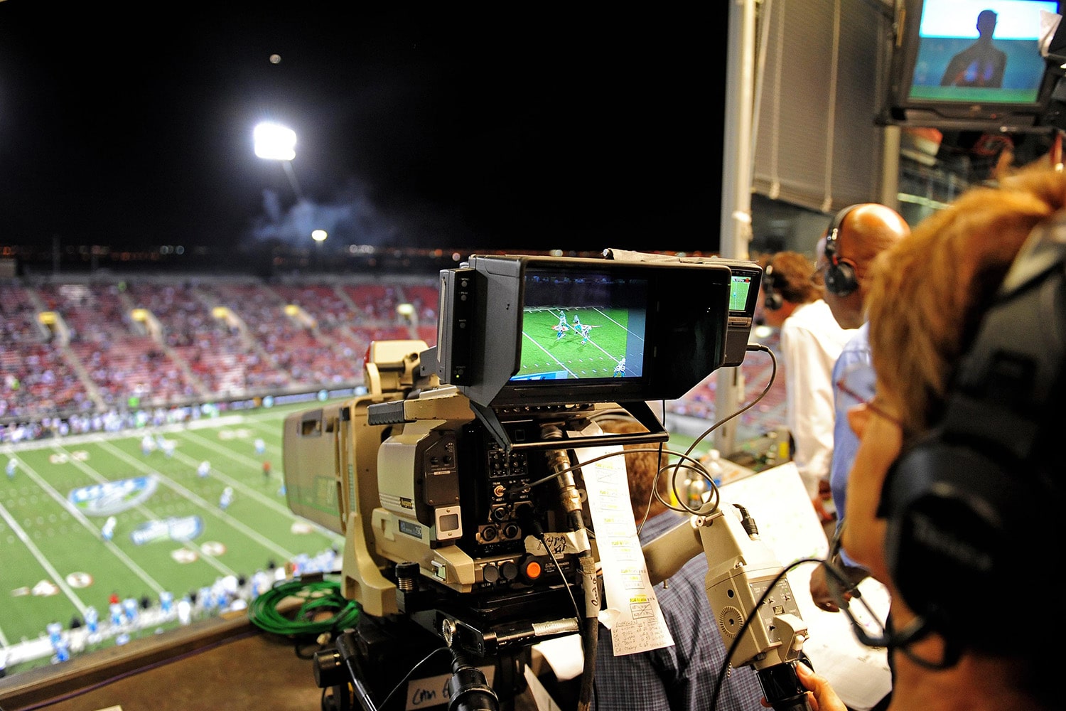 Person operating large camera and recording a football game from the press box