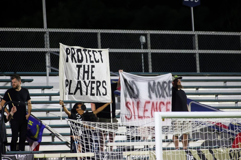 NWSL fans holding signs reading "No more silence" and "respect the players" in response to reports of misconduct by coaches against players