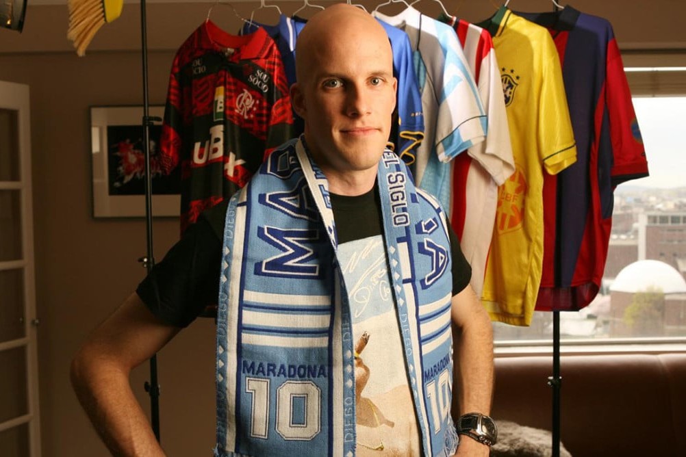 American soccer journalist Grant Wahl wears scarf and poses for photo in front of soccer jerseys