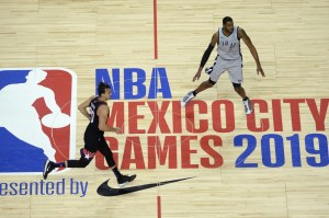 San Antonio Spurs and Phoenix Suns players run past half court in front of NBA Mexico City game logo in 2019