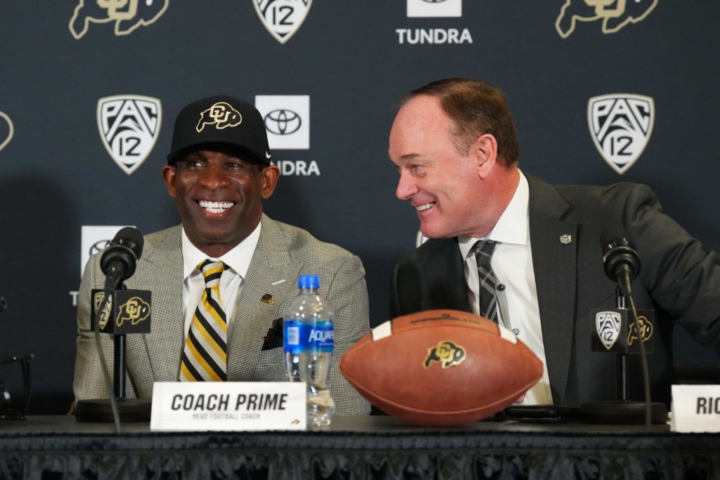 Athletic Director Rick George sits with Deion Sanders as the new Colorado football head coach is announced