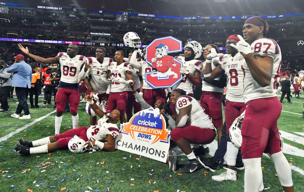 South Carolina State players celebrate in front of bowl game poster after beating Deion Sanders in his last game as Jackson State head coach in Celebration Bowl