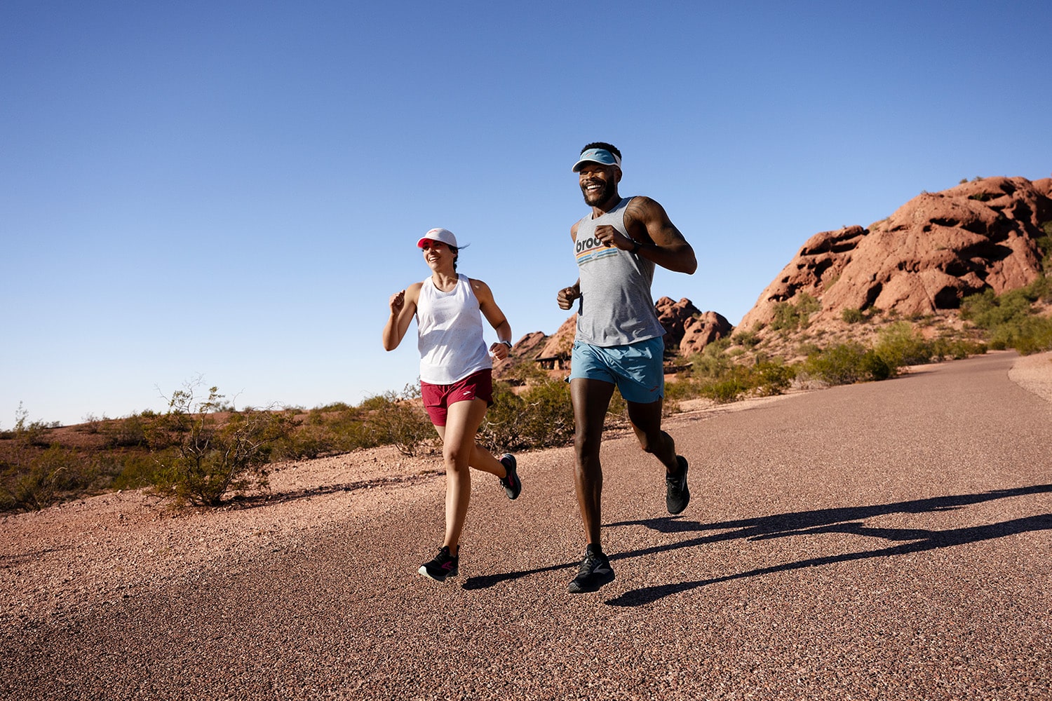 Two runners, wearing Brooks Running apparel and footwear, jogging on a road in the desert.