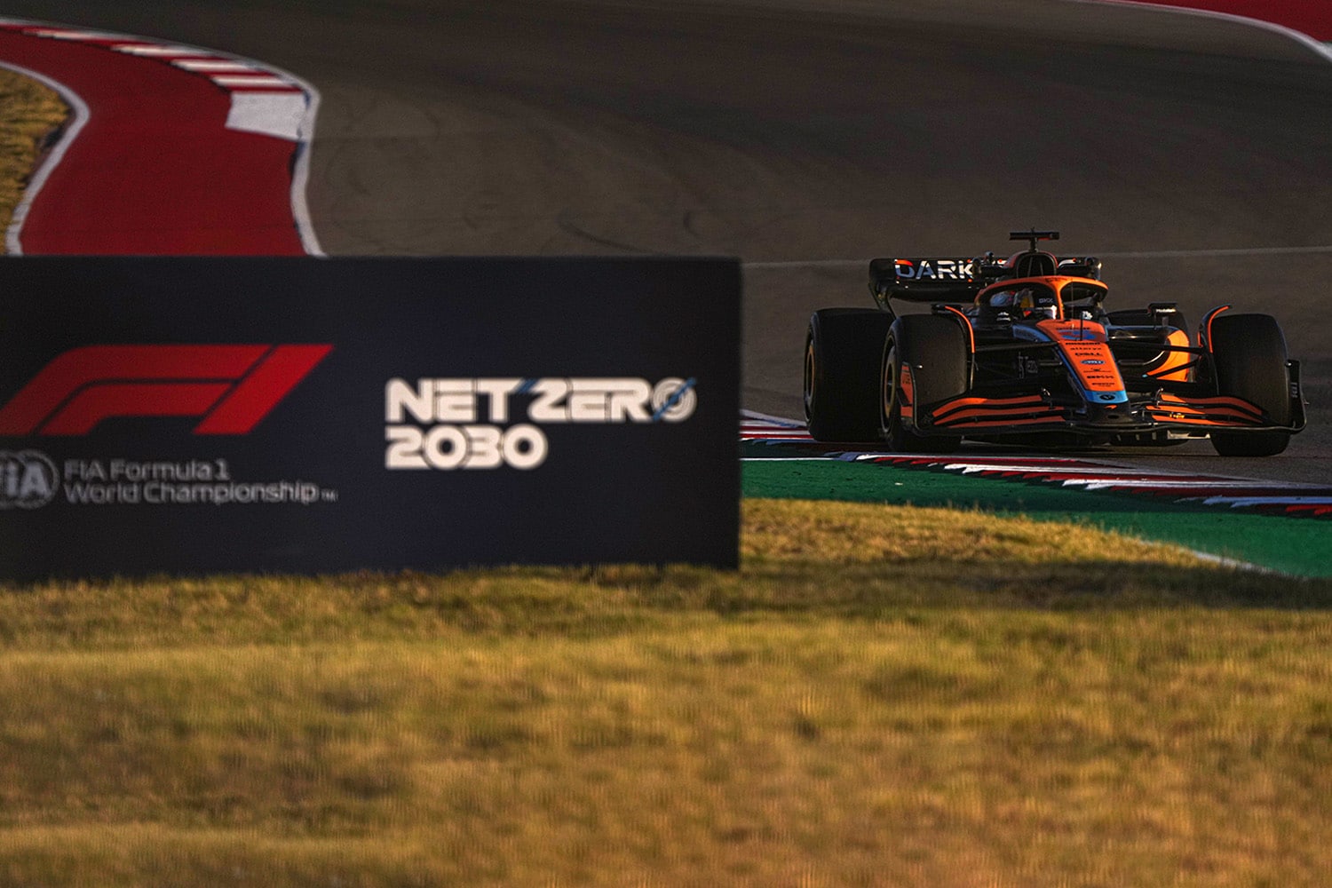 The McLaren F1 car drives past a sign for the FIA's F1 Net Zero 2030 initiative.