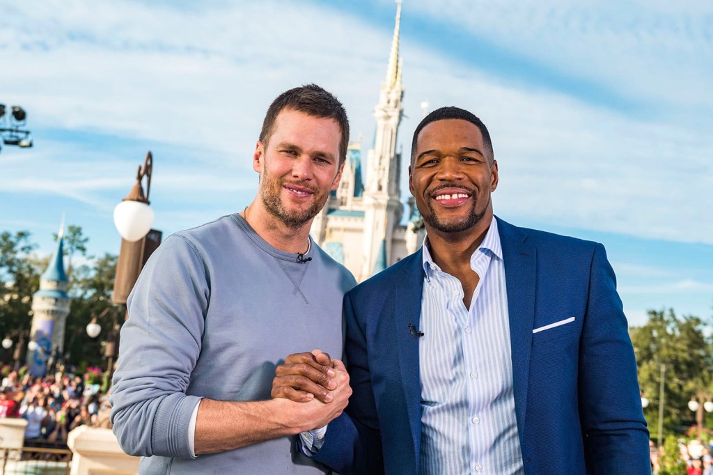 Tom Brady and Michael Strahan pose together while shaking hands.