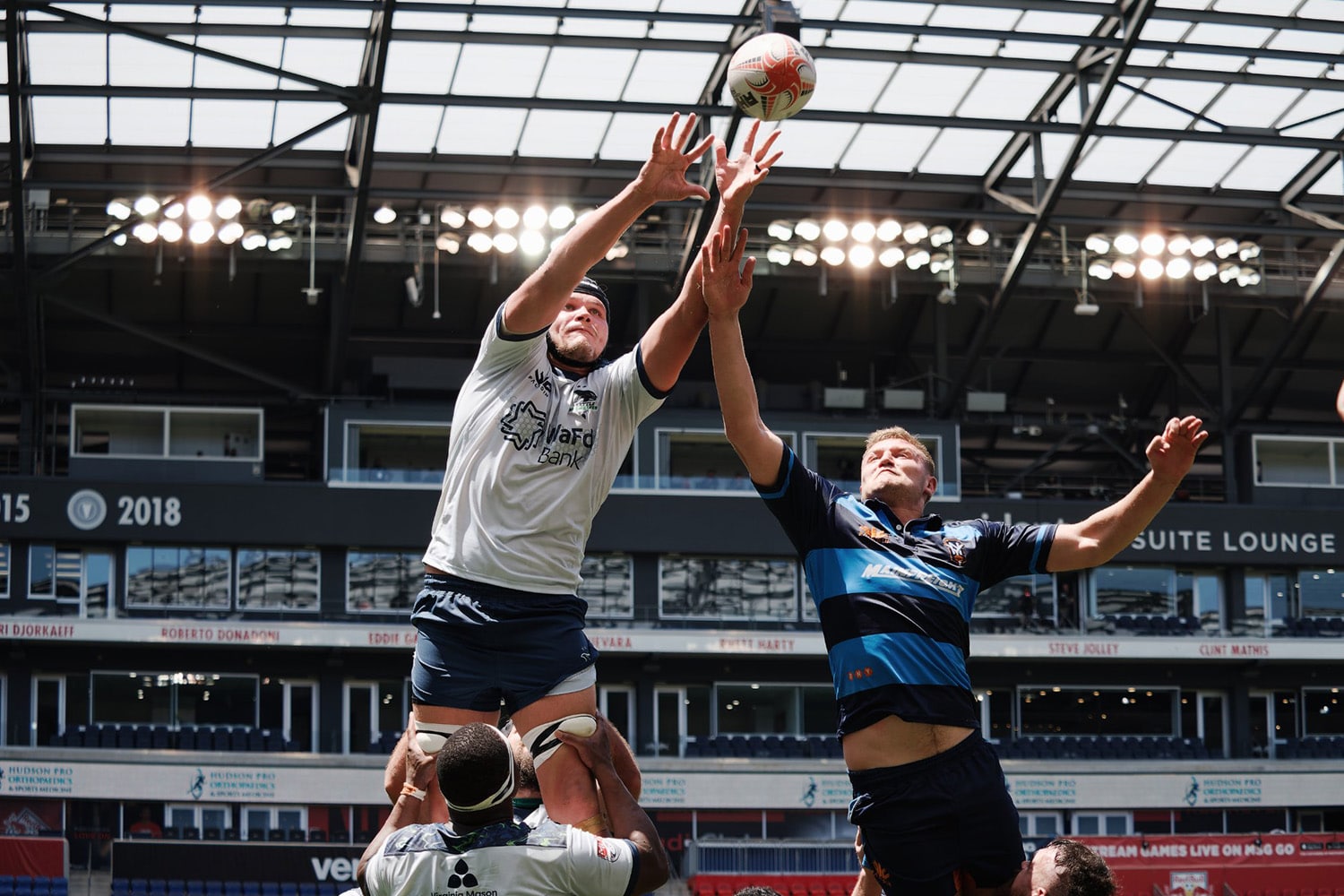 Two Major League Rugby players contest for the ball in the air during play.