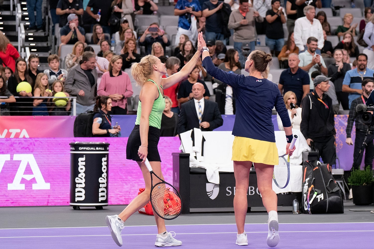 Two WTA players celebrate their doubles win with a high-five.
