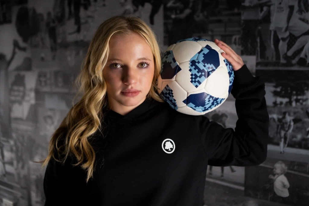 Chloe Ricketts posing while holding a soccer ball on her shoulder.