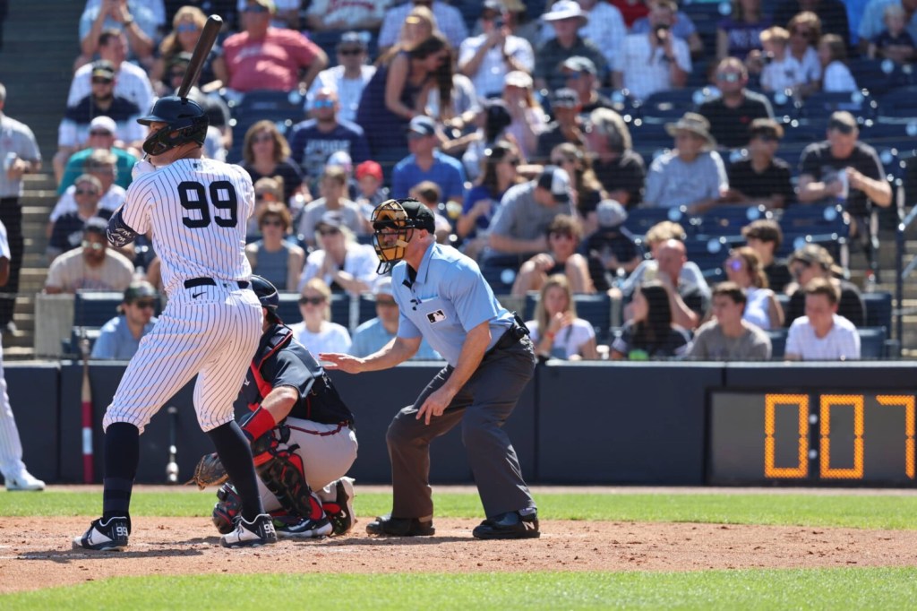 The New York Yankees' Aaron Judge bats during MLB spring training with the pitch clock in the background.