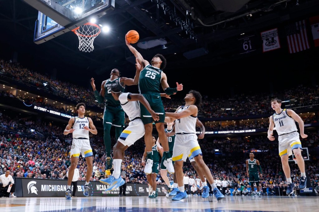 A Michigan State basketball player drives the rim against Marquette in the men's March Madness tournament.