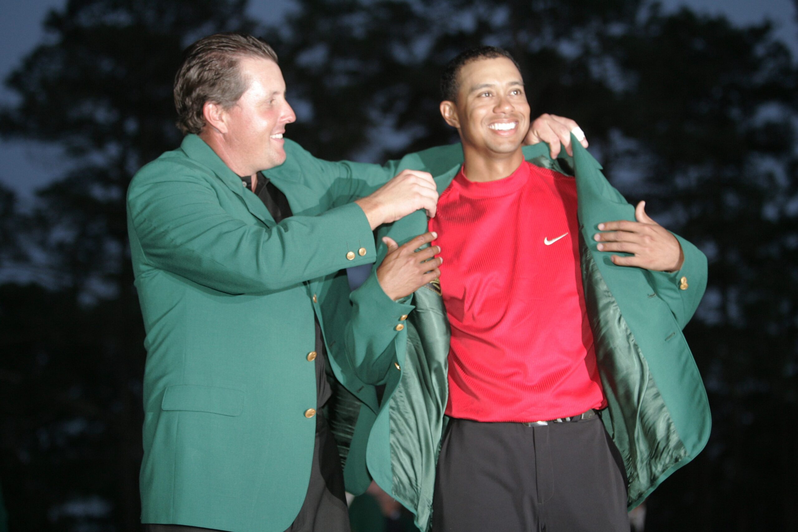 2004 Masters champion Phil Mickelson helps 2005 winner, Tiger Woods, into his fourth green jacket on April 10, 2005.