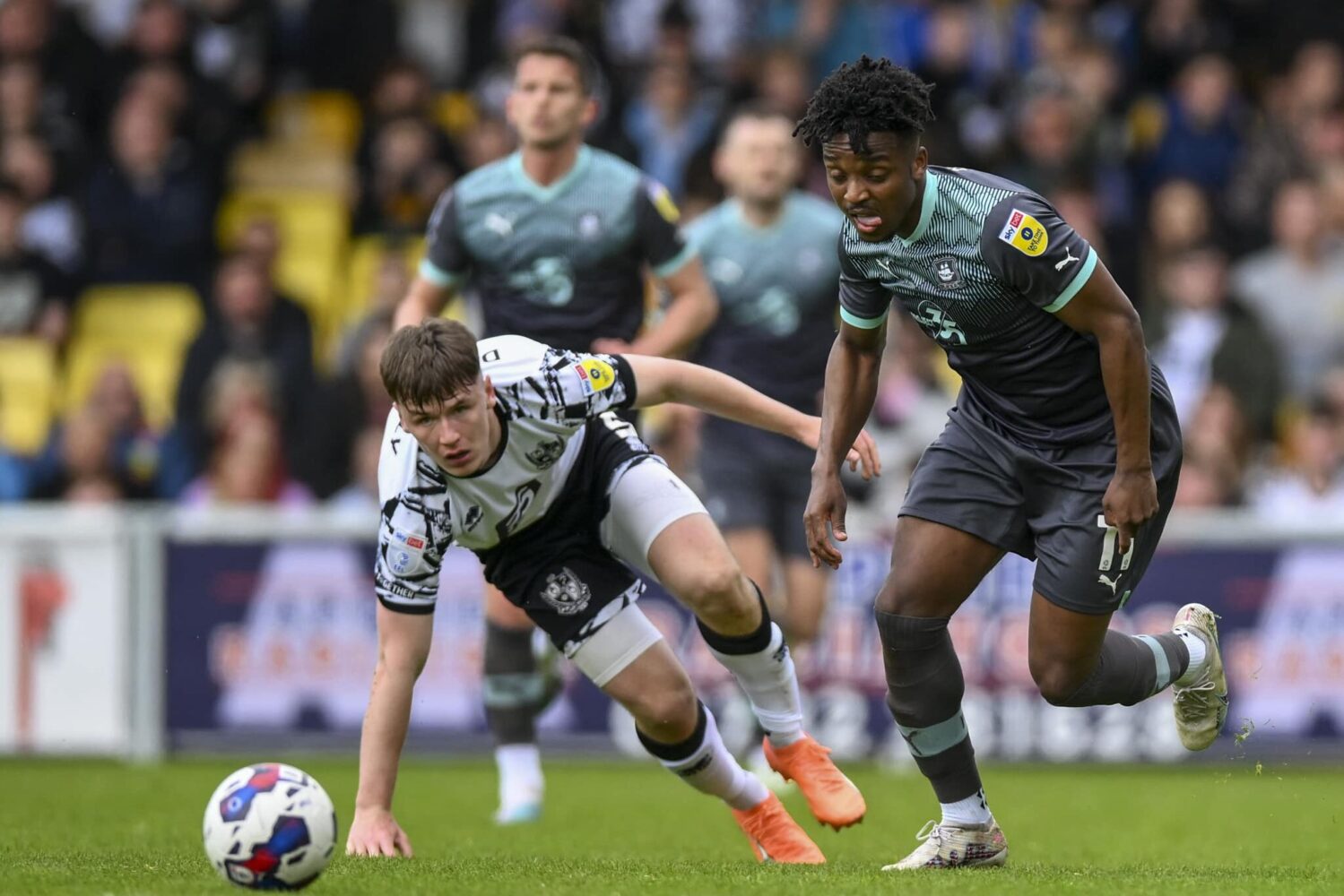 A Port Vale FC and Plymouth Argyle FC player contest for a loose ball during a soccer match.