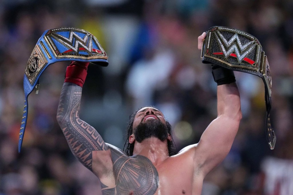 Roman Reigns lifts WWE championship belts during Wrestlemania.