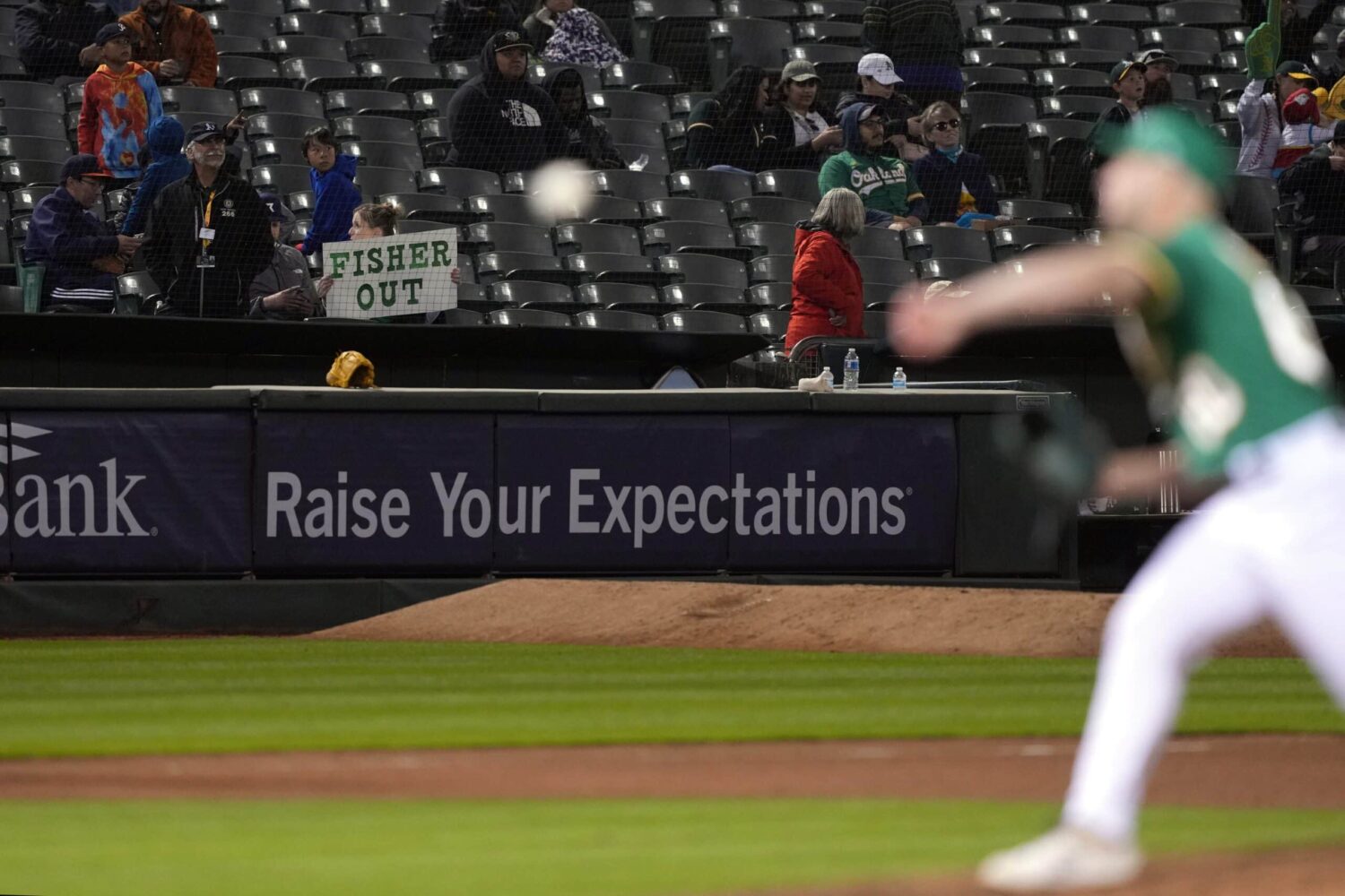 A Oakland Athletics fan holds up a sign directed at owner John Fisher as relief pitcher Sam Moll (foreground) warms up during the eighth inning against the Texas Rangers at Oakland-Alameda County Coliseum.