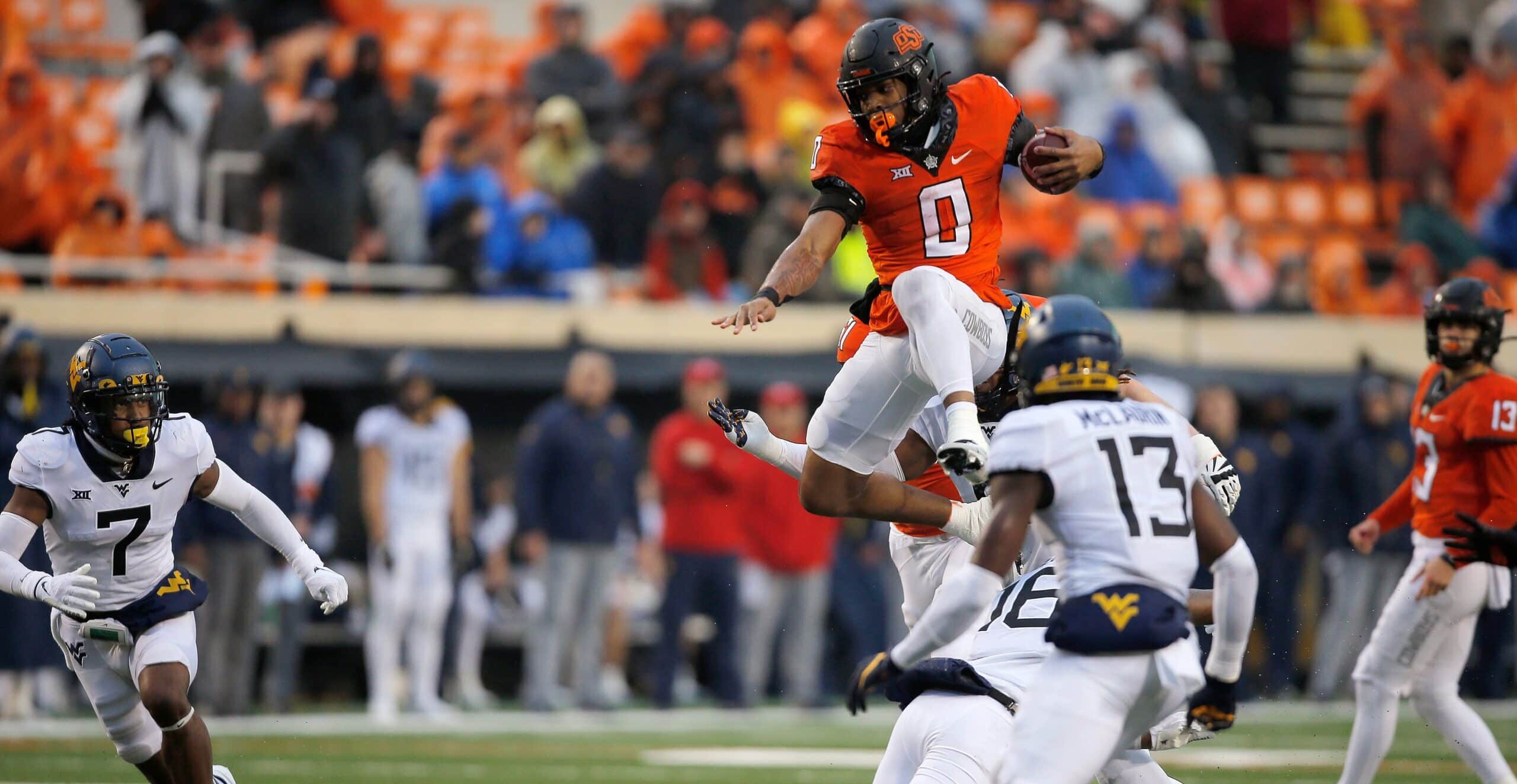 Oklahoma State Cowboys running back Ollie Gordon (0) leaps over West Virginia Mountaineers defensive back Caleb Coleman (16) during a college football game between Oklahoma State and West Virginia at Boone Pickens Stadium.
