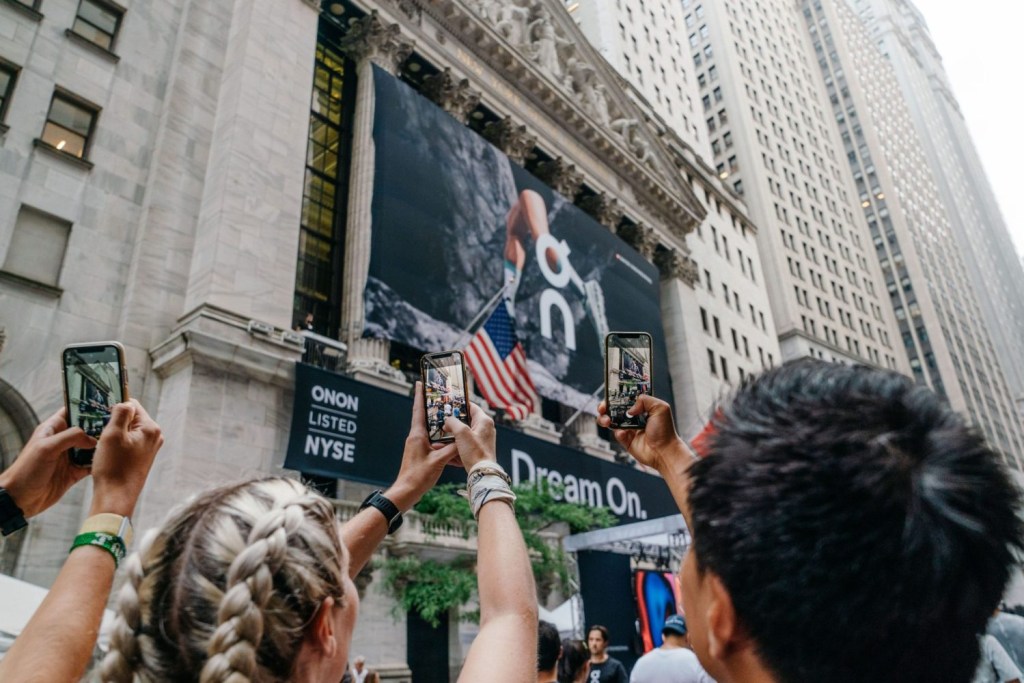 People take pictures on their phones of the New York Stock Exchange decorated with On branding.