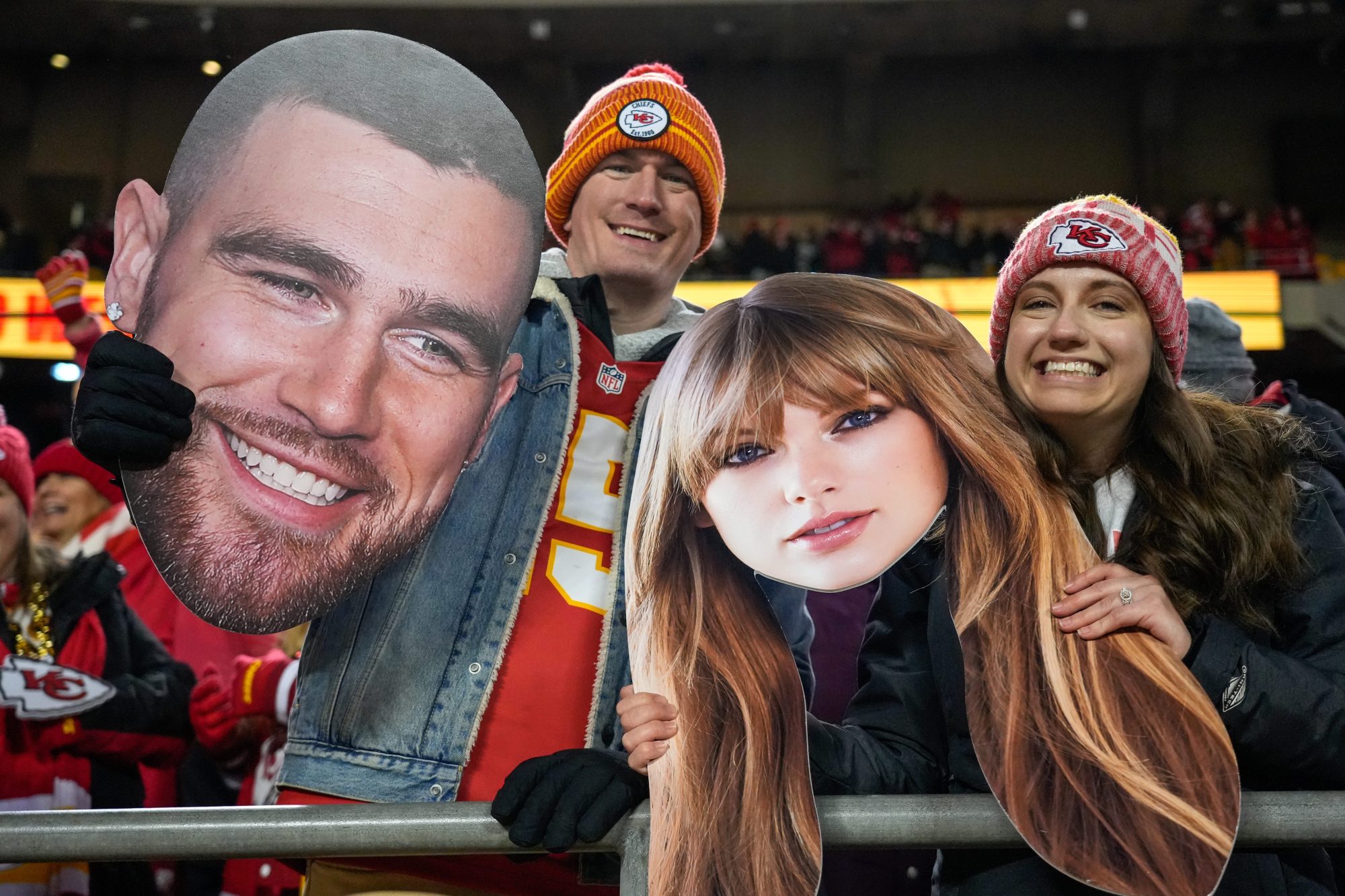 Chiefs fans wave Taylor Swift and Travis Kelce cutouts at Arrowhead Stadium.