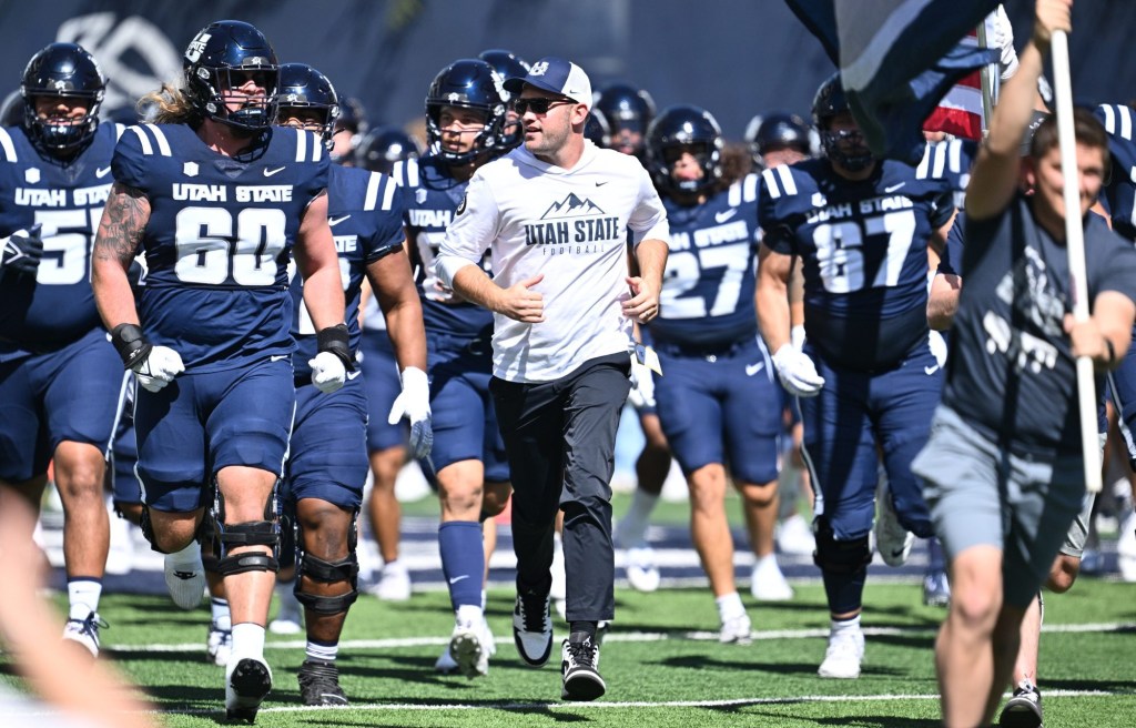 Sep 14, 2024; Logan, Utah, USA; Utah State Aggies interim head coach Nate Dreiling leads his team out onto the field before playing against the Utah Utes at Merlin Olsen Field at Maverik Stadium.