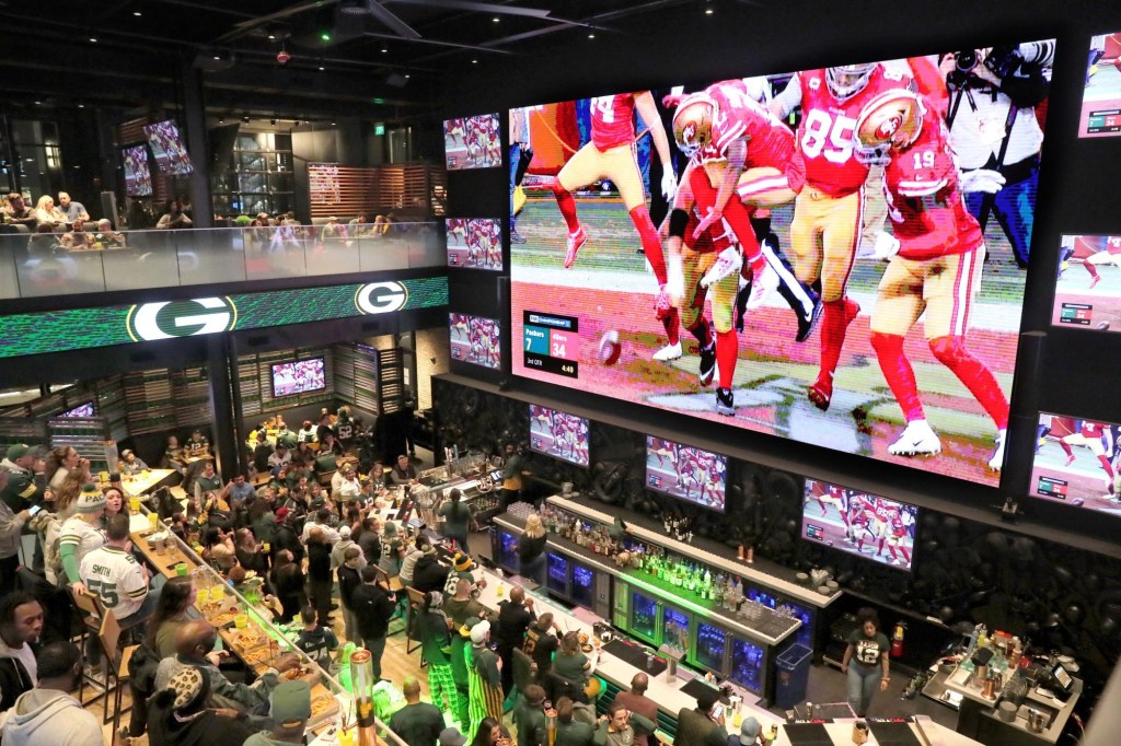 Packers fans watch as the 49ers celebrate one of their touchdowns on a giant TV screen at Mecca Sports Bar and Grill on Jan. 19, 2020.