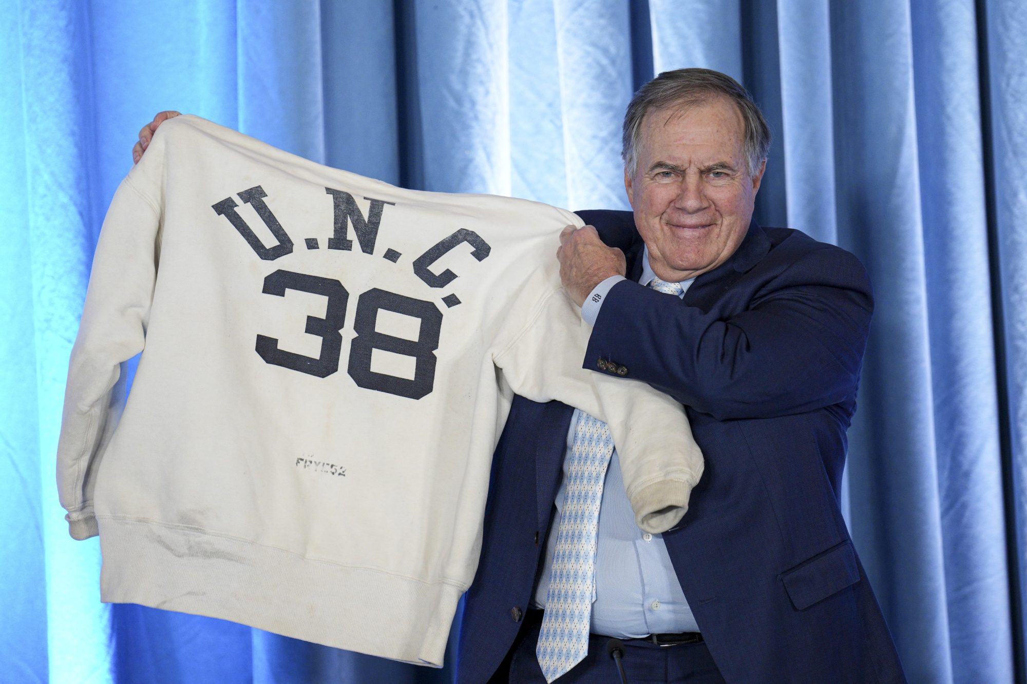 Dec 12, 2024; Chapel Hill, NC, USA; North Carolina Tar Heels new head coach Bill Belichick holds up the sweatshirt worn by his father when he was an assistant coach at New North Carolina Tar Heels new at Loudermilk Center for Excellence.