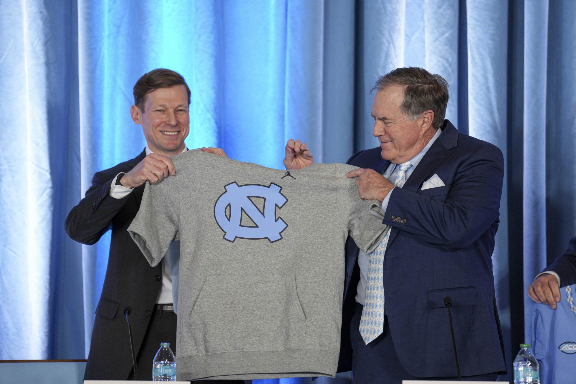 Dec 12, 2024; Chapel Hill, NC, USA; North Carolina Tar Heels chancellor Lee Roberts presents a cut off sweatshirt to new head coach Bill Belichick at Loudermilk Center for Excellence.