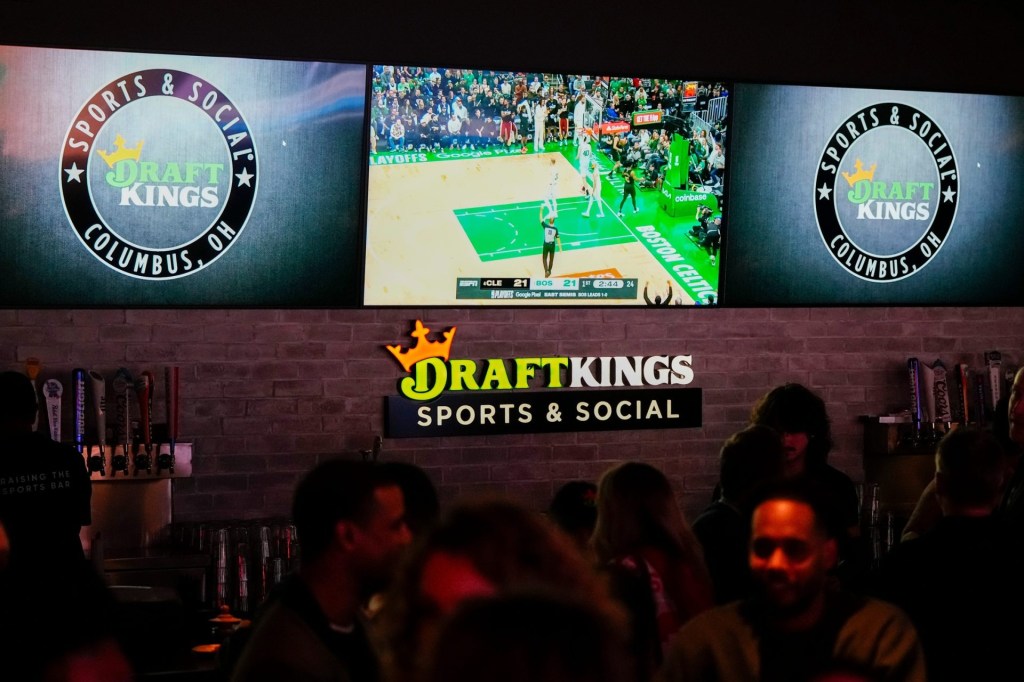 Sports are shown on TVs behind a bar as guests enjoy the grand opening of DraftKings Sports & Social in Ohio.