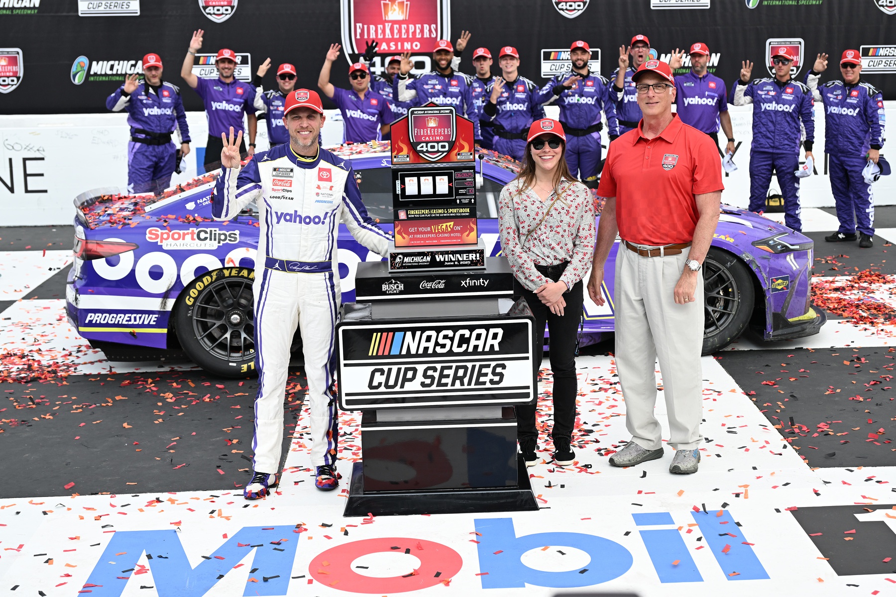 Jun 8, 2025; Brooklyn, Michigan, USA; NASCAR Cup Series driver Denny Hamlin (11) celebrates with his team, holding up three fingers, one for each of his victories at Michigan International Speedway, after winning the FireKeepers Casino 400.