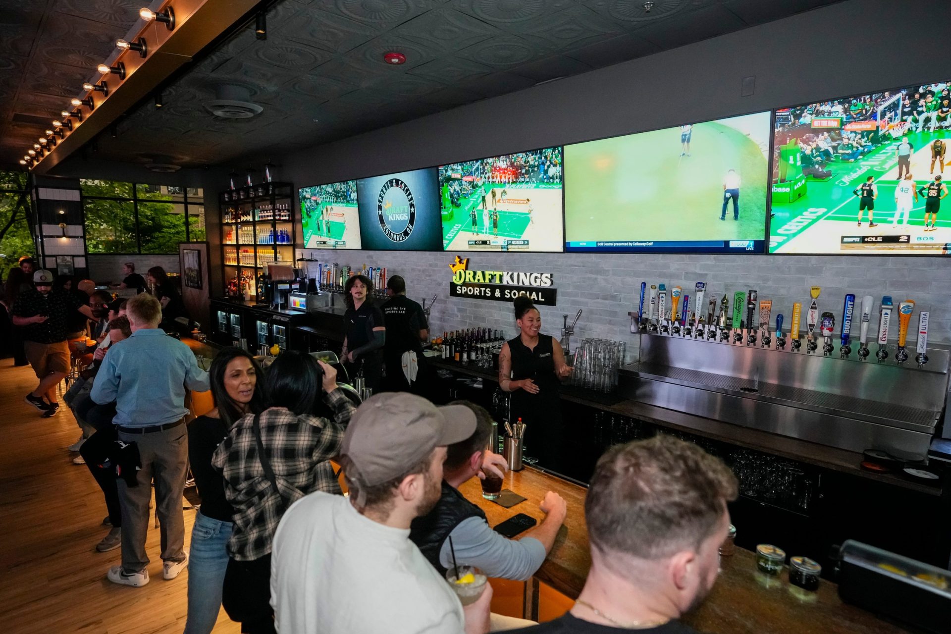 May 9, 2024; Columbus, OH, USA; Sports are shown on TVs behind the bar as guests enjoy the grand opening of DraftKings Sports & Social in the Short North. Though there are no on-site betting windows, eligible customers can place bets through the DraftKings app.