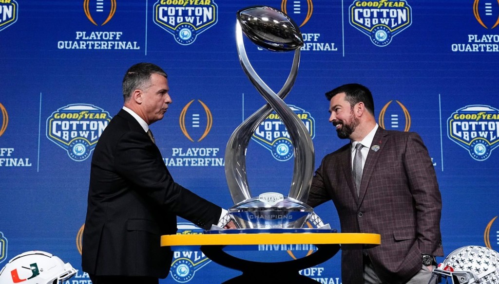 Ohio State Buckeyes head coach Ryan Day, right, and Miami (FL) Hurricanes head coach Mario Cristobal shake hands behind the Field Scovell Trophy after talking to media during a Cotton Bowl press conference at AT&T Stadium in Arlington, Texas prior to their College Football Playoff quarterfinal matchup on Dec. 30, 2025.