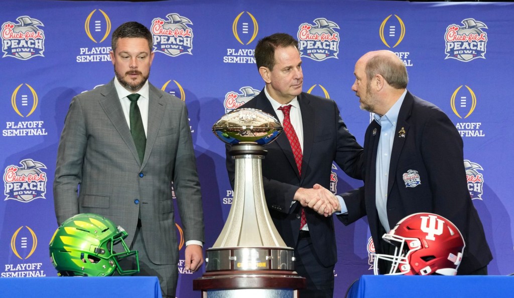 Oregon Ducks head coach Dan Lanning and Indiana Hoosiers head coach Curt Cignetti shake hands with Gary Stokan on Thursday, Jan. 8, 2026, during a coaches' press conference ahead of the College Football Playoff Peach Bowl game at the College Football Hall of Fame in Atlanta.