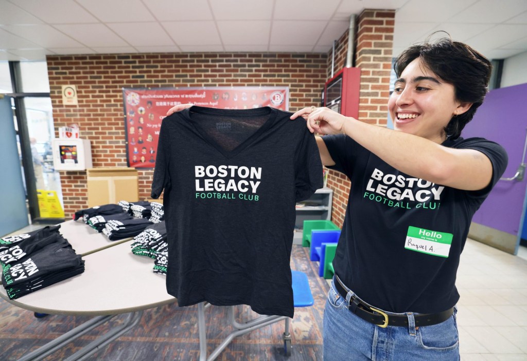 Raquel Aguiree displays a Boston Legacy shirt at a neighborhood meeting on Saturday, May 31, 2025, at Brookfield School to discuss the pro women's soccer team's draft plans for a training facility in Brockton in the old Removal Park area.