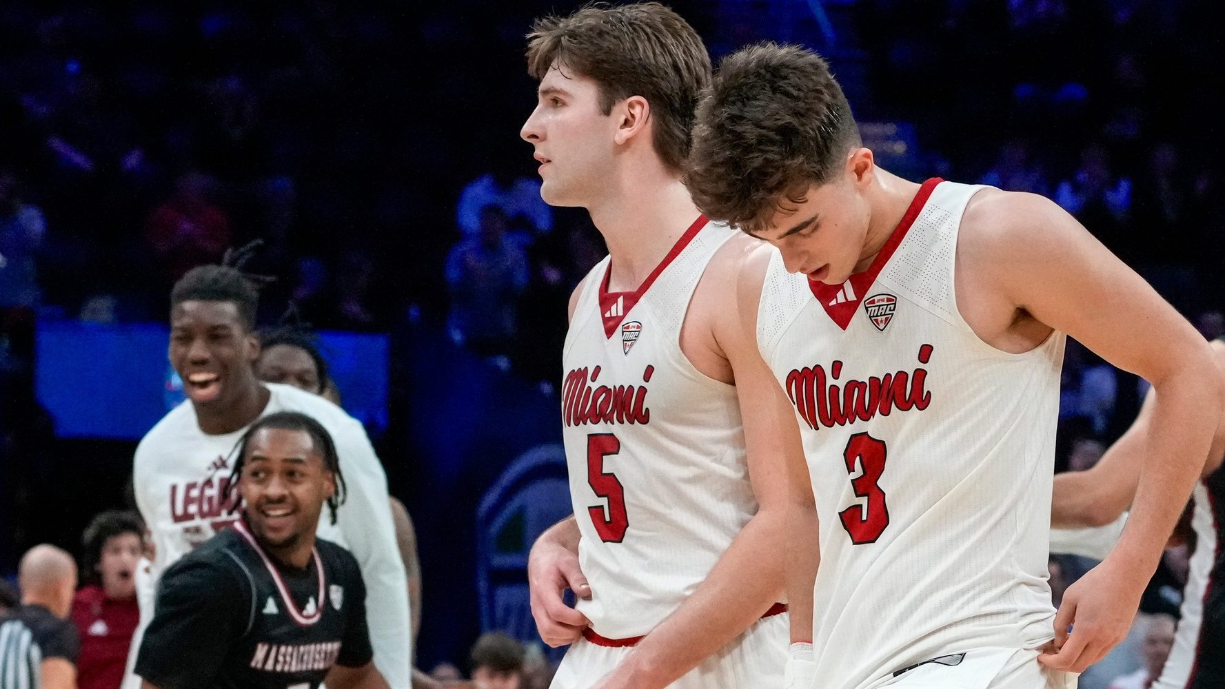 Miami RedHawks guard Peter Suder (5) and guard Luke Skaljac (3) leave the floor as UMass Minutemen forward Leonardo Bettiol (3) celebrates a win after the final buzzer of the second half of Mid-American Conference Tournament first round game between the Miami RedHawks and the UMass Minutemen at Rocket Arena in Cleveland on Thursday, March 12, 2026. Top-seeded Miami was eliminated from the tournament with an 87-82 loss to the Minutemen.