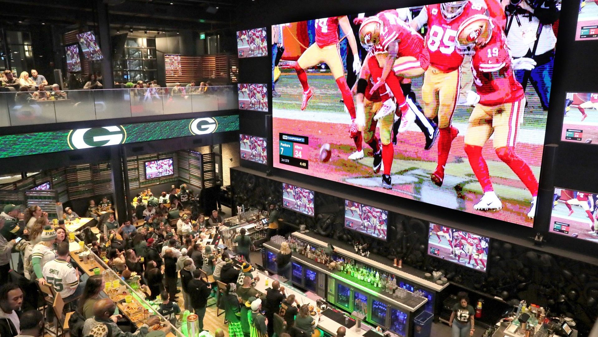 Packers fans watch as the 49ers celebrate one of their touchdowns on a giant TV screen at Mecca Sports Bar and Grill on Jan. 19, 2020.