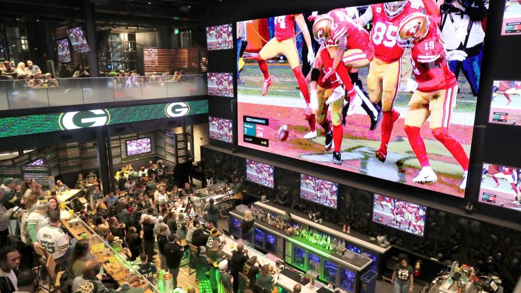 Packers fans watch as the 49ers celebrate one of their touchdowns on a giant TV screen at Mecca Sports Bar and Grill on Jan. 19, 2020.