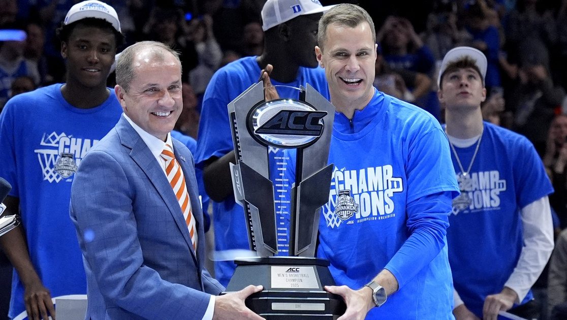 Mar 15, 2025; Charlotte, NC, USA; ACC commissioner Jim Phillips hands the championship trophy to Duke Blue Devils head coach Jon Scheyer after the 2025 ACC Conference Championship game against the Louisville Cardinals at Spectrum Center. Mandatory Credit: Jim Dedmon-Imagn Images