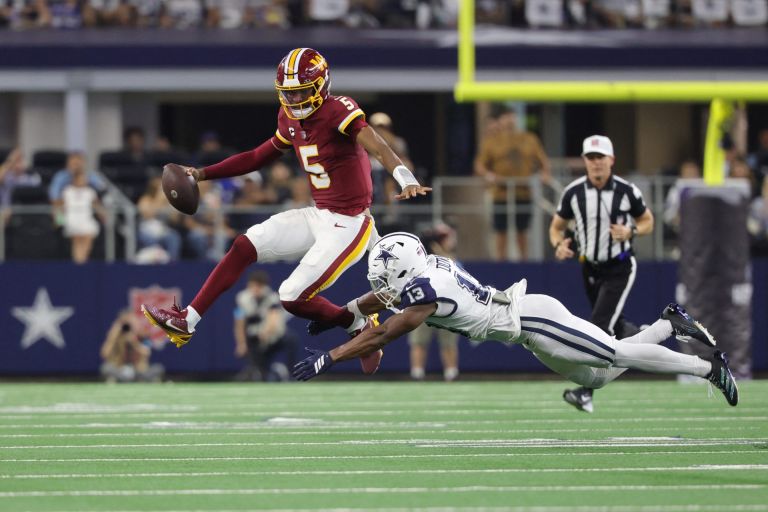 Sep 20, 2026; Arlington, Texas, USA; Washington Commanders quarterback Jayden Daniels (5) leaps to avoid a tackle by Dallas Cowboys safety Caleb Downs (13) while running with the ball during the second half at AT&T Stadium.