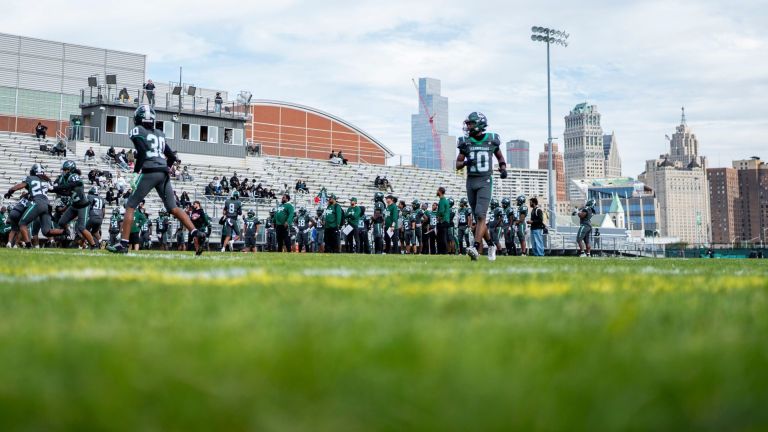 Detroit Cass Tech players warm up ahead of a high school football game against rival Detroit King at Cass Technical High School in Detroit on Friday, Sept. 25, 2026. The Detroit skyline is seen in the background.